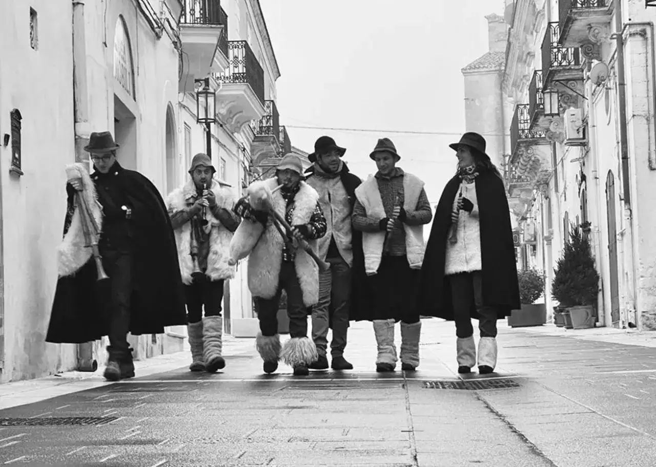 Un gruppo di musicisti con le piva piva suona per le strade di un borgo antico, vestiti con abiti tradizionali e cappotti di pelliccia.