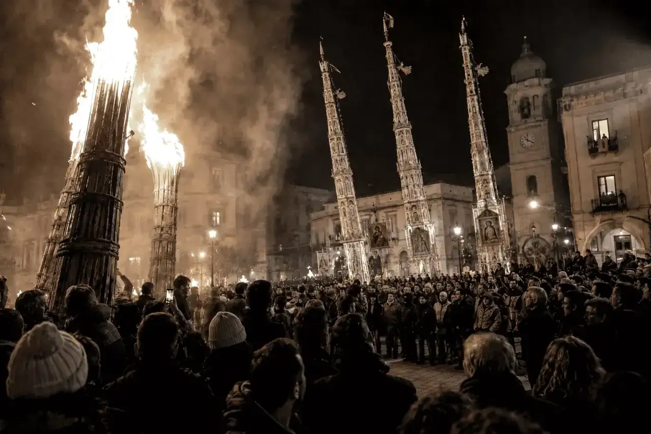 Fiamme alte illuminano una piazza gremita, con torri decorate e un'atmosfera che evoca un antico significato pagano.