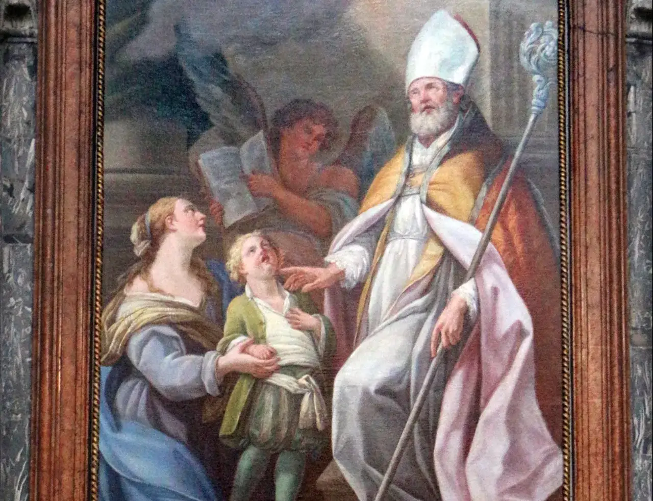 San Biagio, con mitra e pastorale, benedice un bambino, mentre un angelo legge. Il significato del nome Biagio è