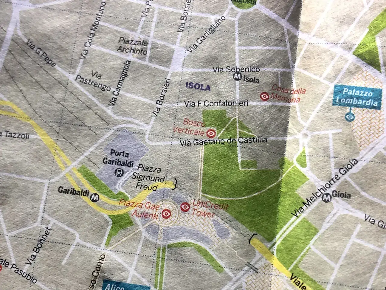 Mappa di Milano con zone come Isola, Bosco Verticale, Porta Garibaldi e Piazza Gae Aulenti. Nomi di strade e luoghi che richiamano la storia e i cognomi milanesi.