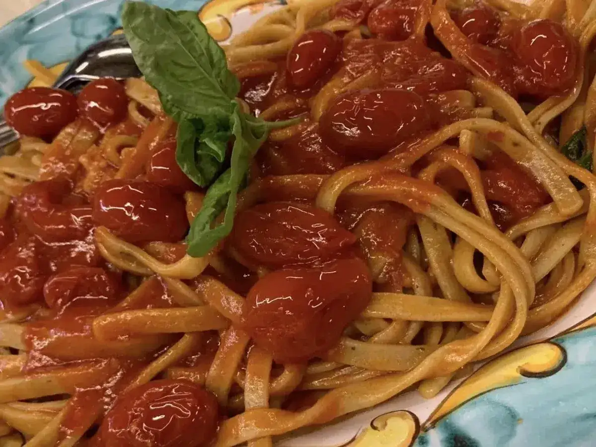 Un piatto di pasta con un sugo rosso vivo, arricchito da pomodorini pachino succosi e una foglia di basilico fresco.