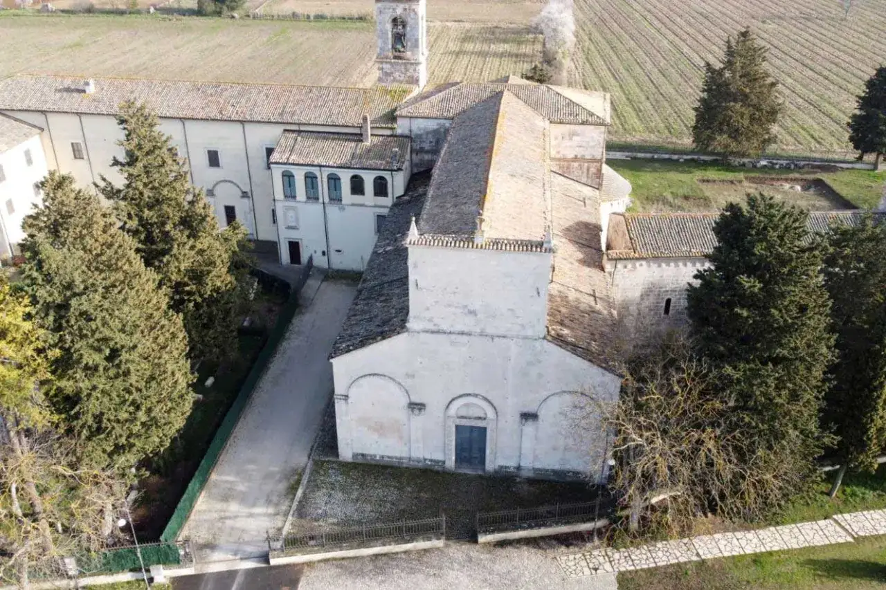 Vista aerea del complesso monastico di San Pelino a Corfinio, con la chiesa romanica e il campanile che si stagliano tra alberi secolari e campi coltivati.