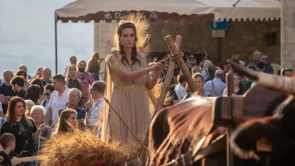 Donna in abito dorato, con spighe di grano che simboleggiano abbondanza e fertilità, durante una festa popolare.