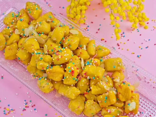 Dolcezza dorata: la ricetta cicerchiata marchigiana, decorata con confettini colorati e mandorle, pronta per essere gustata.