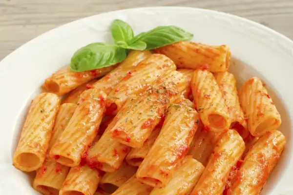 Un piatto di rigatoni al sugo, conditi con erbe aromatiche e guarniti con foglie di basilico fresco. Il maccarone, nella sua semplicità, racchiude un significato di convivialità e tradizione.