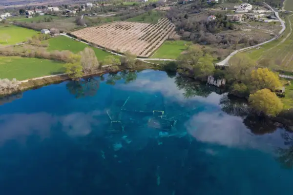 Le rovine sommerse nel lago azzurro evocano un'Atlantide d'Abruzzo. Campi verdi e alberi circondano questo luogo magico.