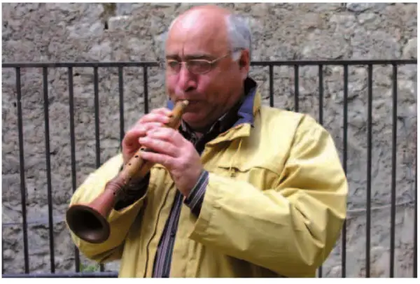Uomo con occhiali suona uno strumento a fiato, una piva, con un suono melodioso.