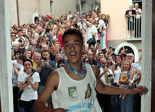 Giovane festante con la maglia "Madonna di Loreto" a Pacentro, tra una folla che filma e applaude.