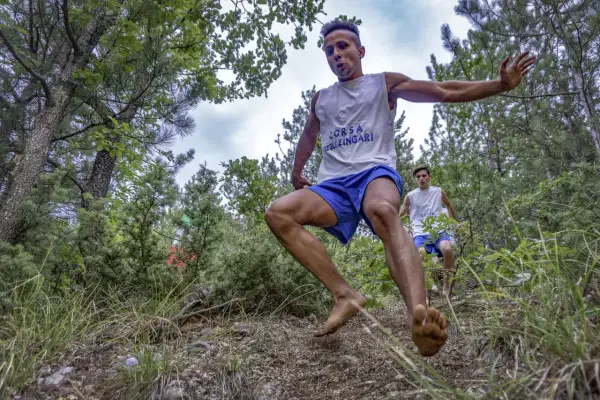 Due giovani atleti corrono a piedi nudi nel bosco, partecipando alla "Corsa degli Zingari". Il primo è in primo piano, in pieno balzo.