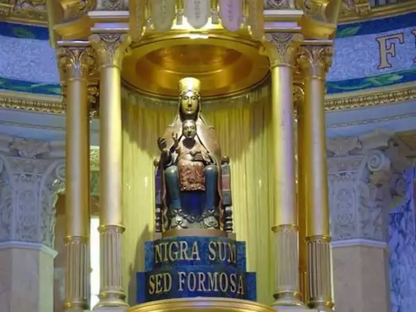 Statua dorata di una Maria nera con Gesù Bambino, su un piedistallo con iscrizione latina.
