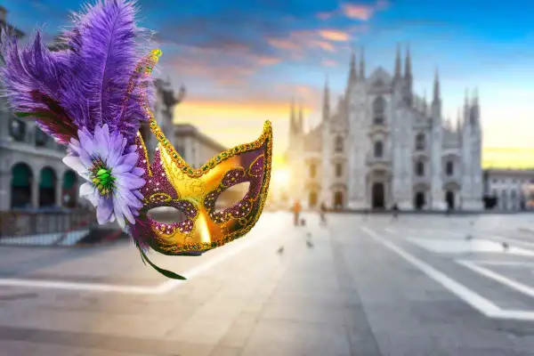 Maschere milanesi decorate con piume e fiori, con il Duomo di Milano sullo sfondo al tramonto.
