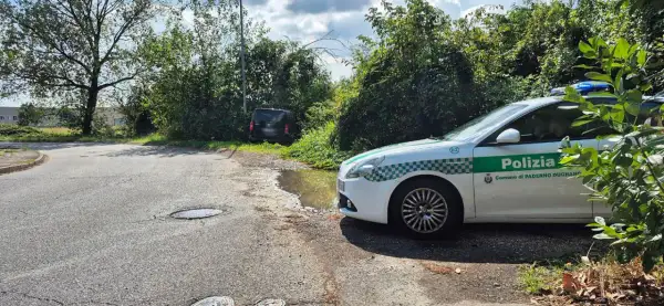 Sei di Paderno Dugnano se vedi la Polizia locale vicino a un'auto nera parcheggiata male e una pozzanghera sull'asfalto.