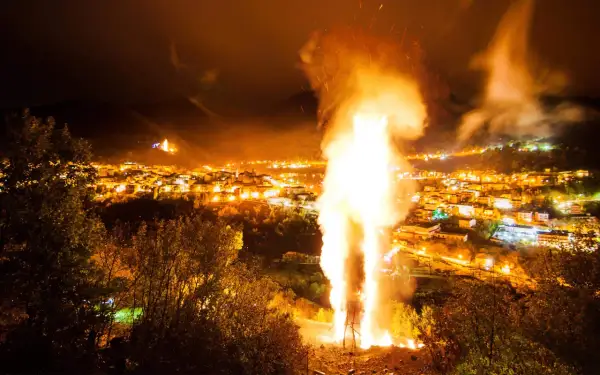 Un imponente falò illumina la notte, celebrando le glorie di San Martino. Le fiamme danzano sopra un villaggio illuminato, creando uno spettacolo magico.