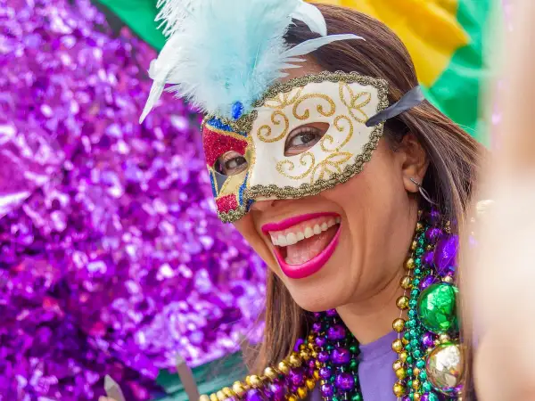 Donna sorridente con maschera di carnevale e perline colorate. L'etimologia di carnevale, "addio alla carne", si riflette nella gioia sfrenata.