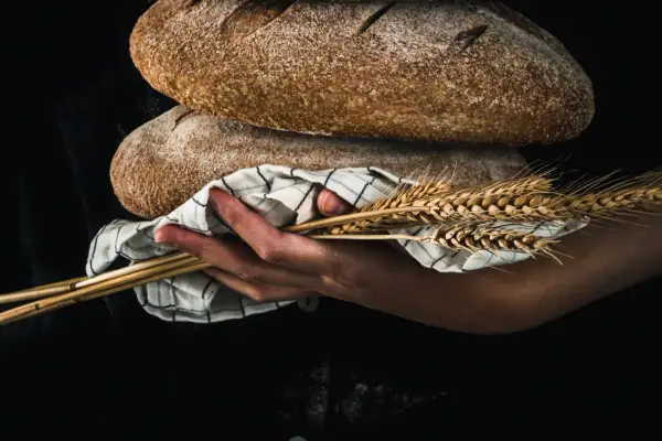 Mani che sorreggono pani rustici e spighe di grano, evocando il significato pagano del raccolto e della fertilità.