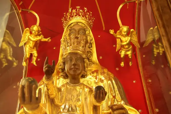 Statua della Madonna Nera, con il Bambino Gesù, circondata da angeli dorati su sfondo rosso.