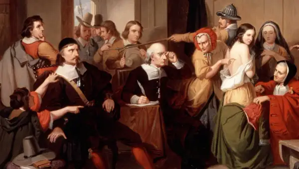 Un gruppo di persone esamina una giovane donna, cercando segni fisici delle streghe. Un uomo scrive, mentre altri osservano con sospetto.