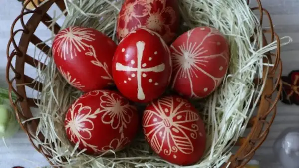 Uova di Pasqua rosse decorate con motivi floreali e una croce, simbolo uovo di Pasqua significato di rinascita e speranza, in un cesto.
