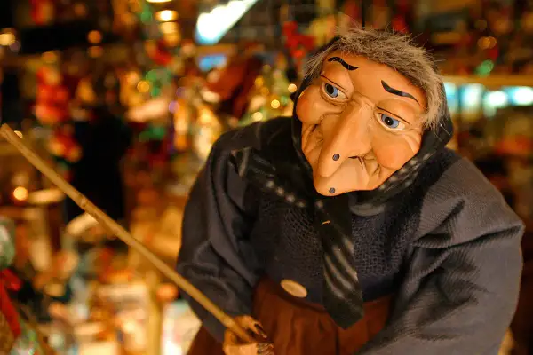 Una bambola di una strega famosa, con un naso adunco e occhi azzurri, tiene una scopa.